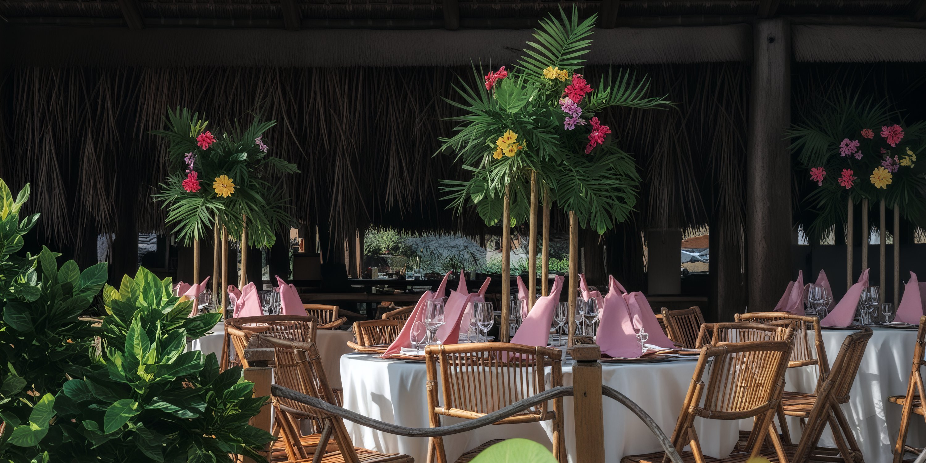 Round tables with pink napkins and tall tropical floral centerpieces set for a destination wedding outdoors.