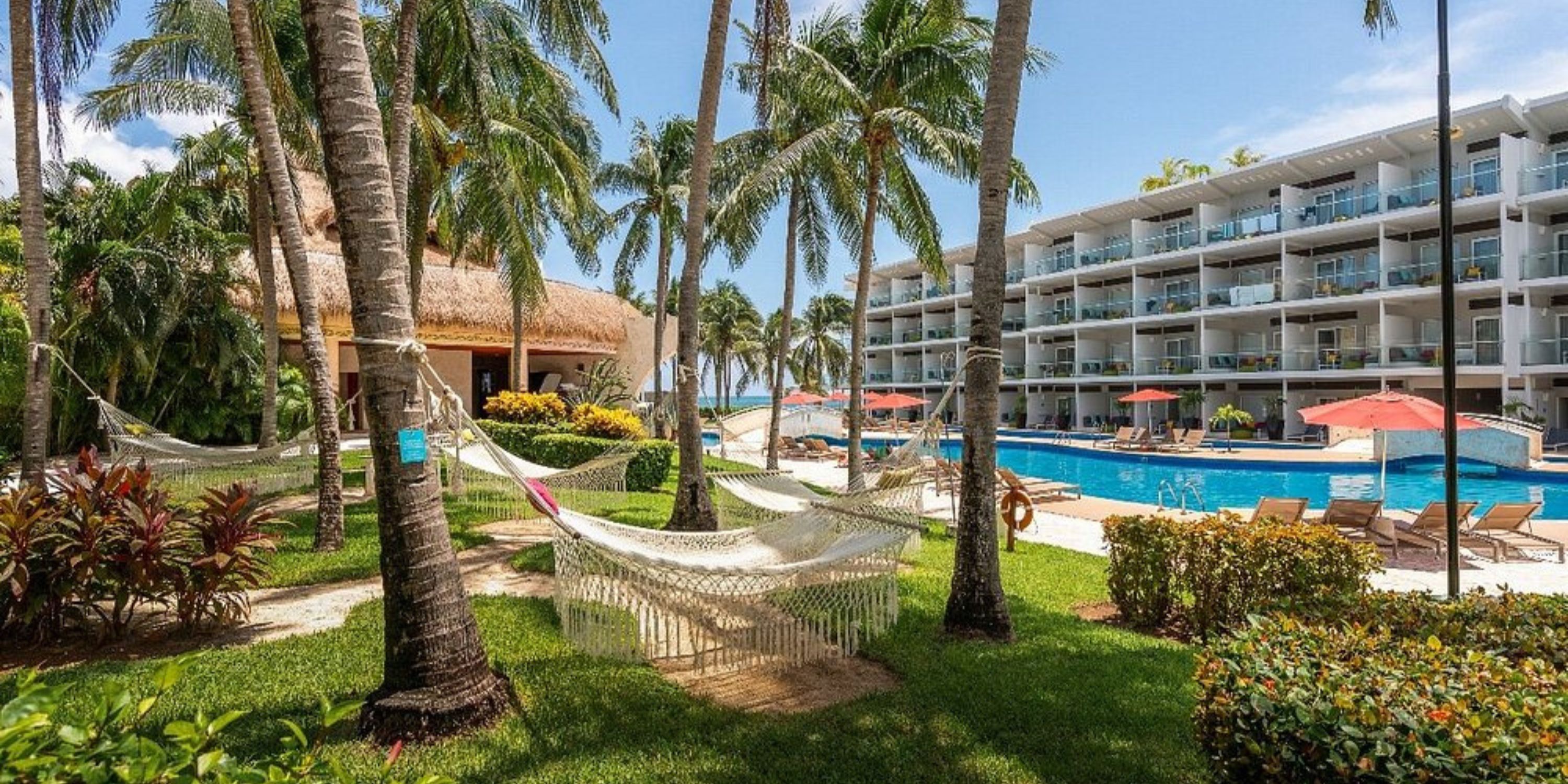 Hammocks by palm trees and pool near modern balconies, ideal for a dreamy destination wedding setting.