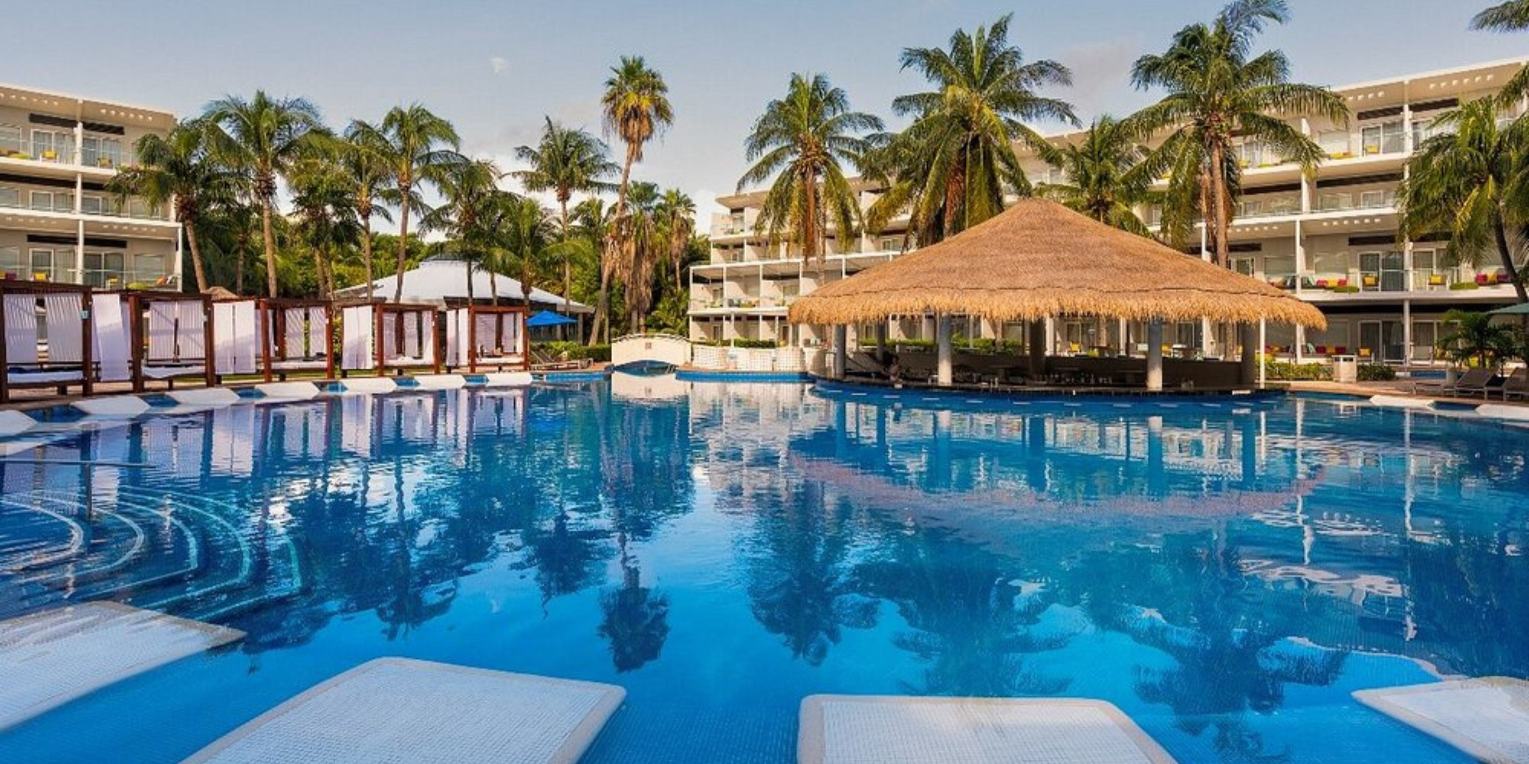 Outdoor pool with thatched-roof bar and lounge chairs, perfect for a destination wedding at Iberostar.
