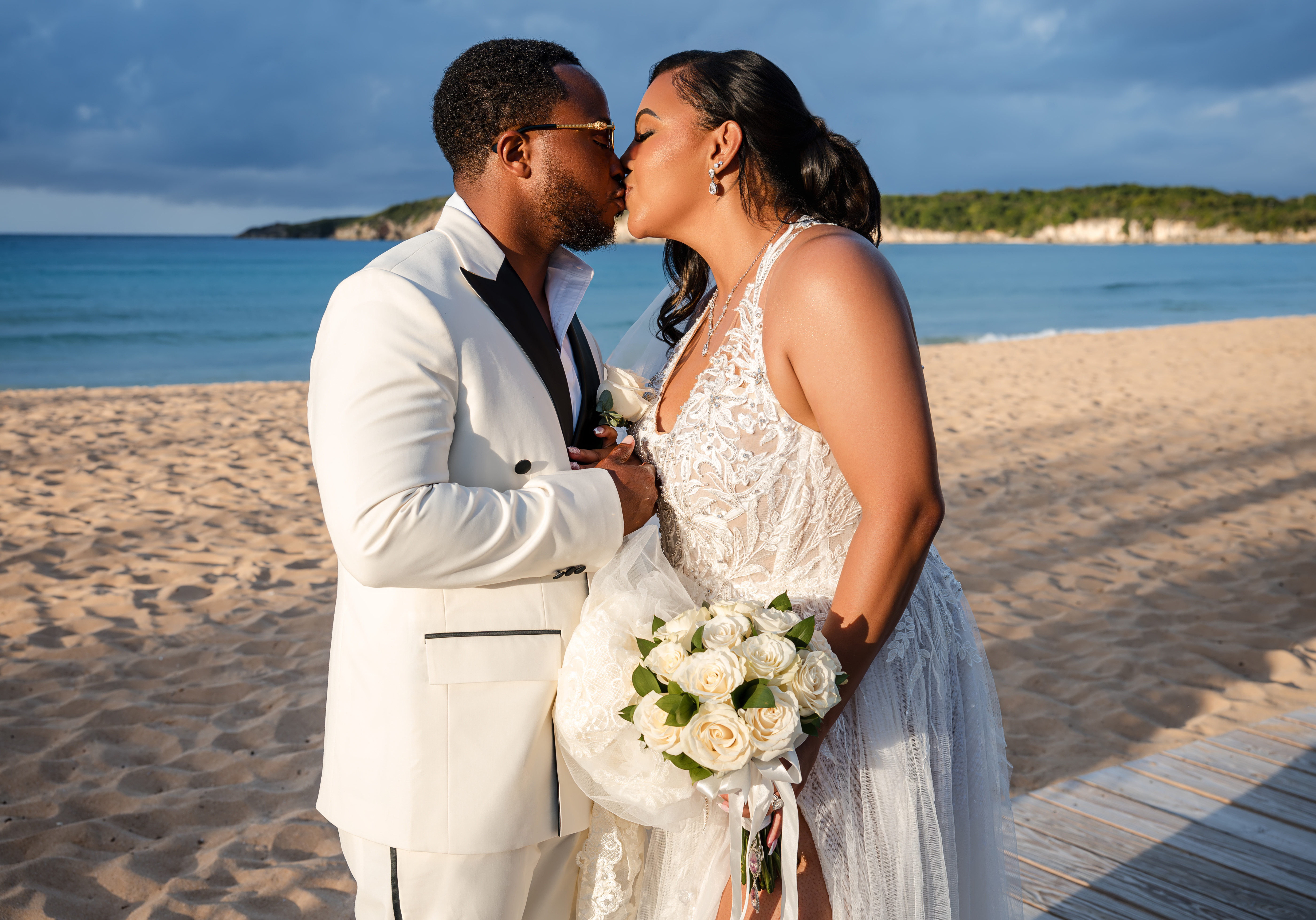 Leah and Ben share a kiss on a sandy beach, dressed in wedding attire at their destination wedding.