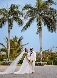 Leah and Ben (Copy) pose together outdoors at their destination wedding, with tall palm trees behind them.