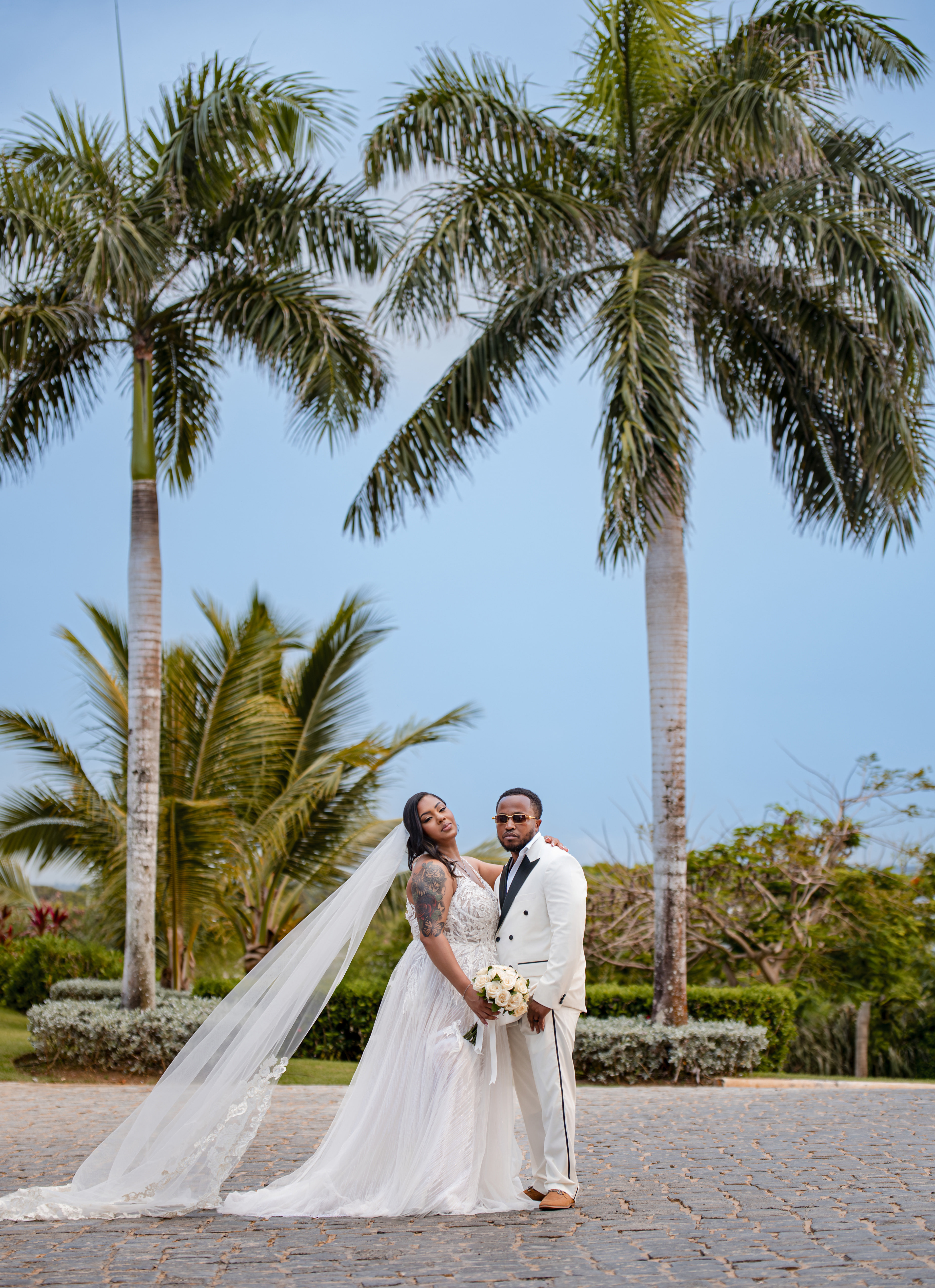 Leah and Ben (Copy) pose together outdoors at their destination wedding, with tall palm trees behind them.