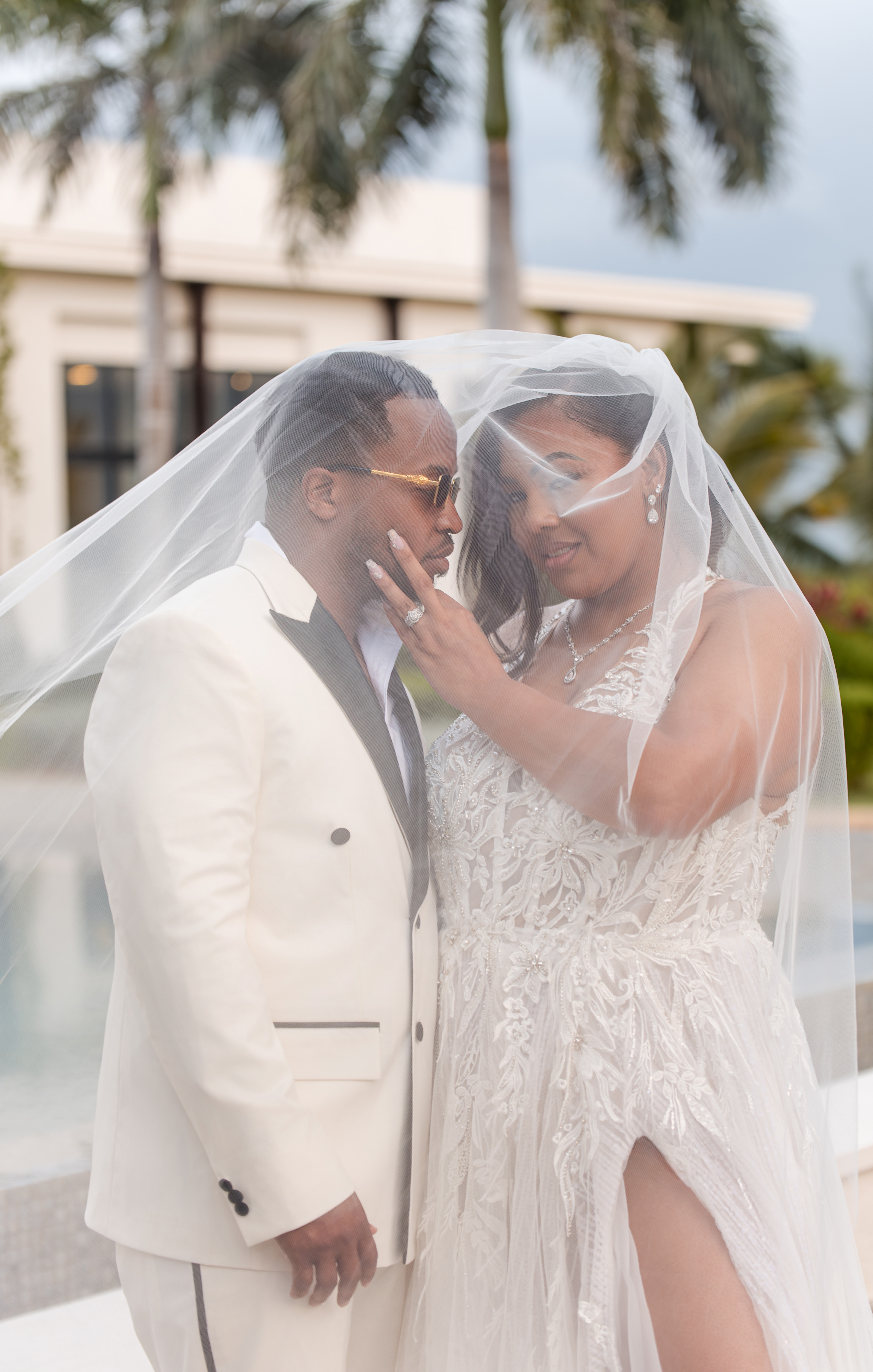 Leah and Ben stand outdoors under a veil in wedding attire at their destination wedding.
