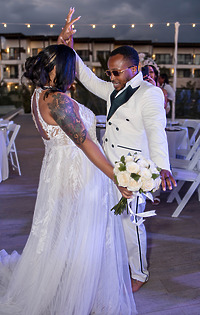 Leah and Ben dance at their destination wedding outdoors; bride holds bouquet, white chairs behind them.