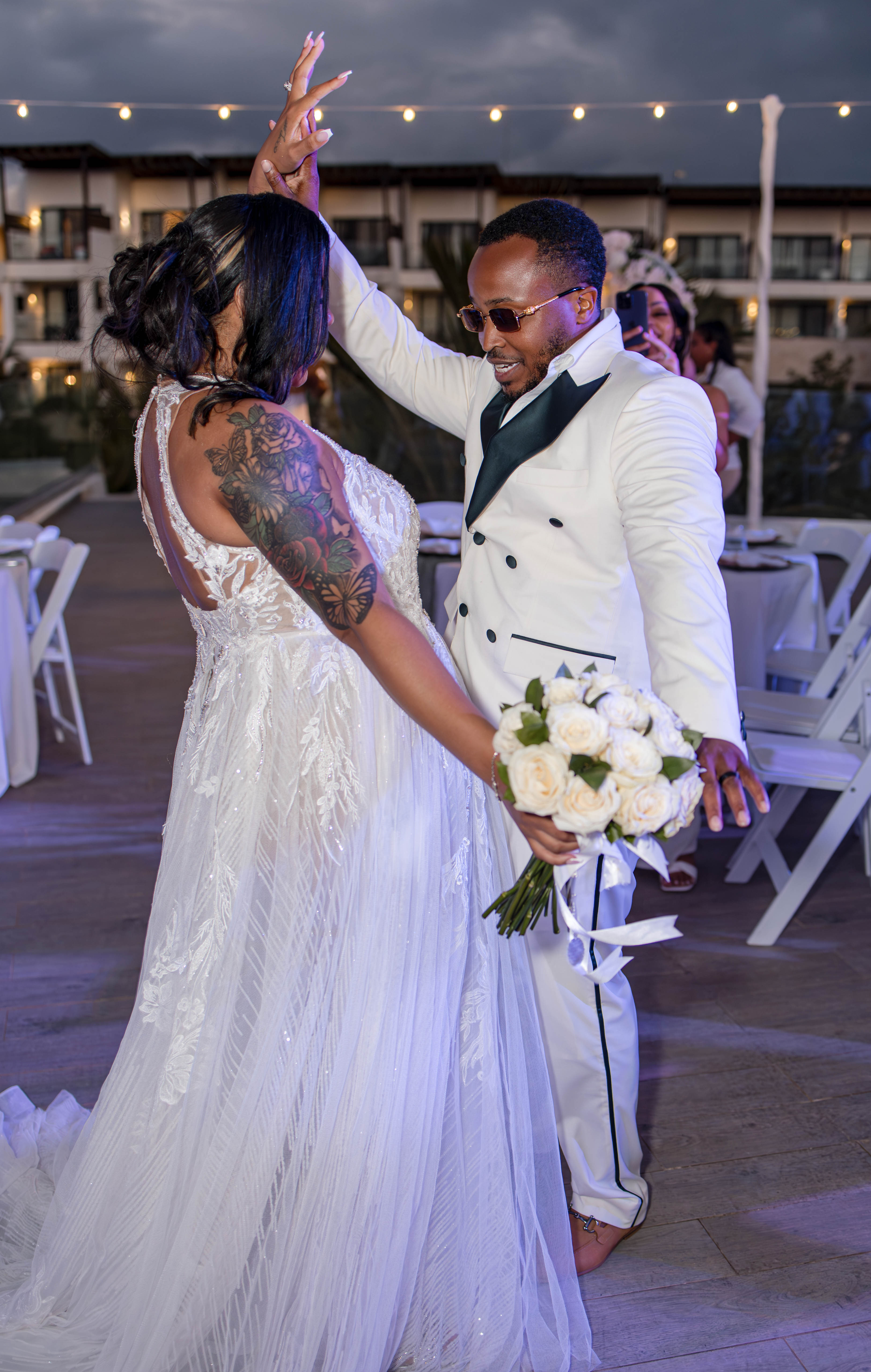 Leah and Ben dance at their destination wedding outdoors; bride holds bouquet, white chairs behind them.