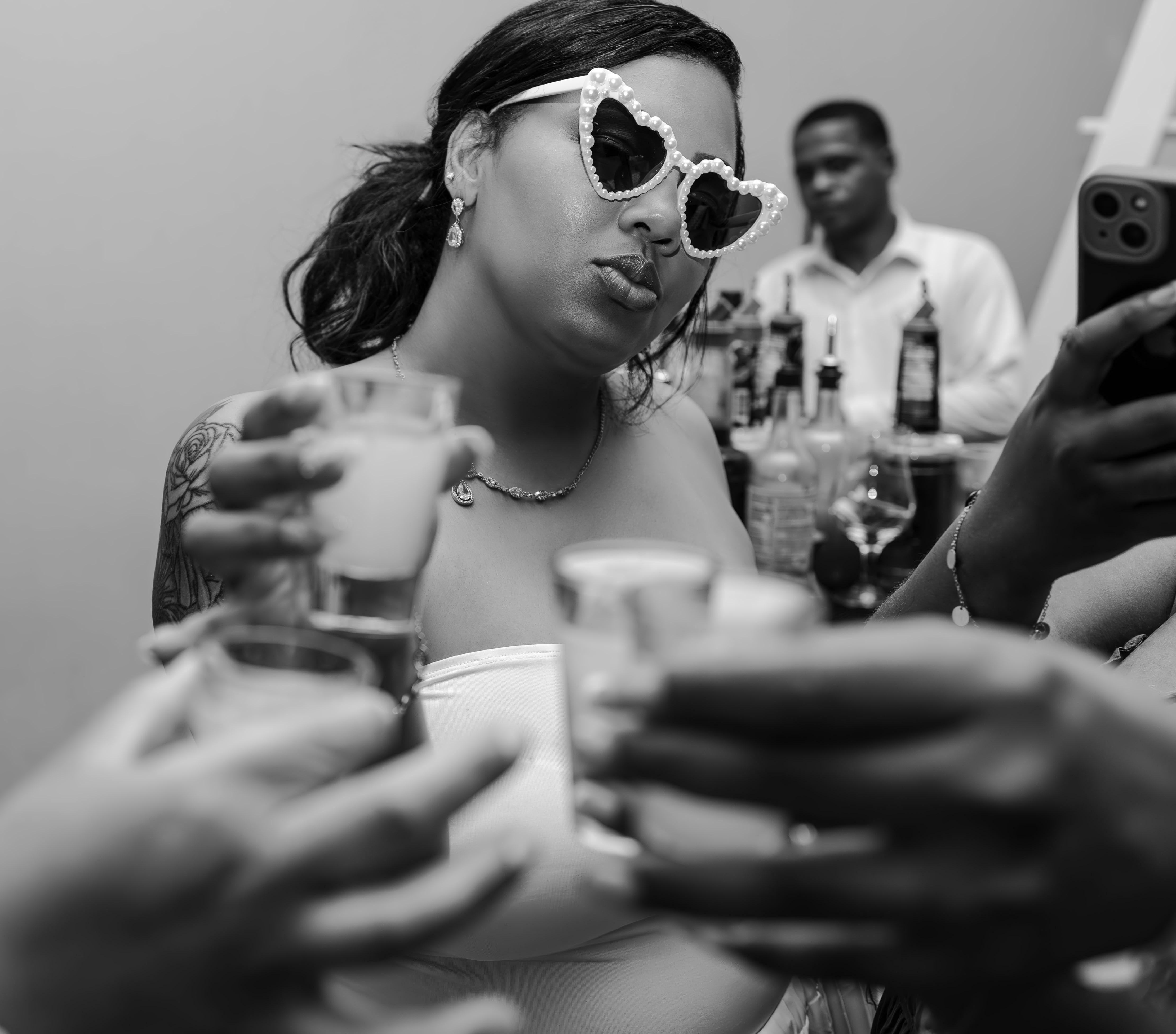 Woman in Leah and Ben (Copy) sunglasses raises a shot glass at a lively destination wedding gathering.