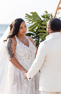 Leah and Ben hold hands in white outfits during their outdoor destination wedding ceremony.