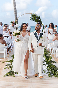Leah and Ben walk down the aisle at their destination wedding on the beach, guests in white attire.