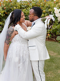Leah and Ben embrace at their destination wedding outdoors, dressed in white and holding white roses.