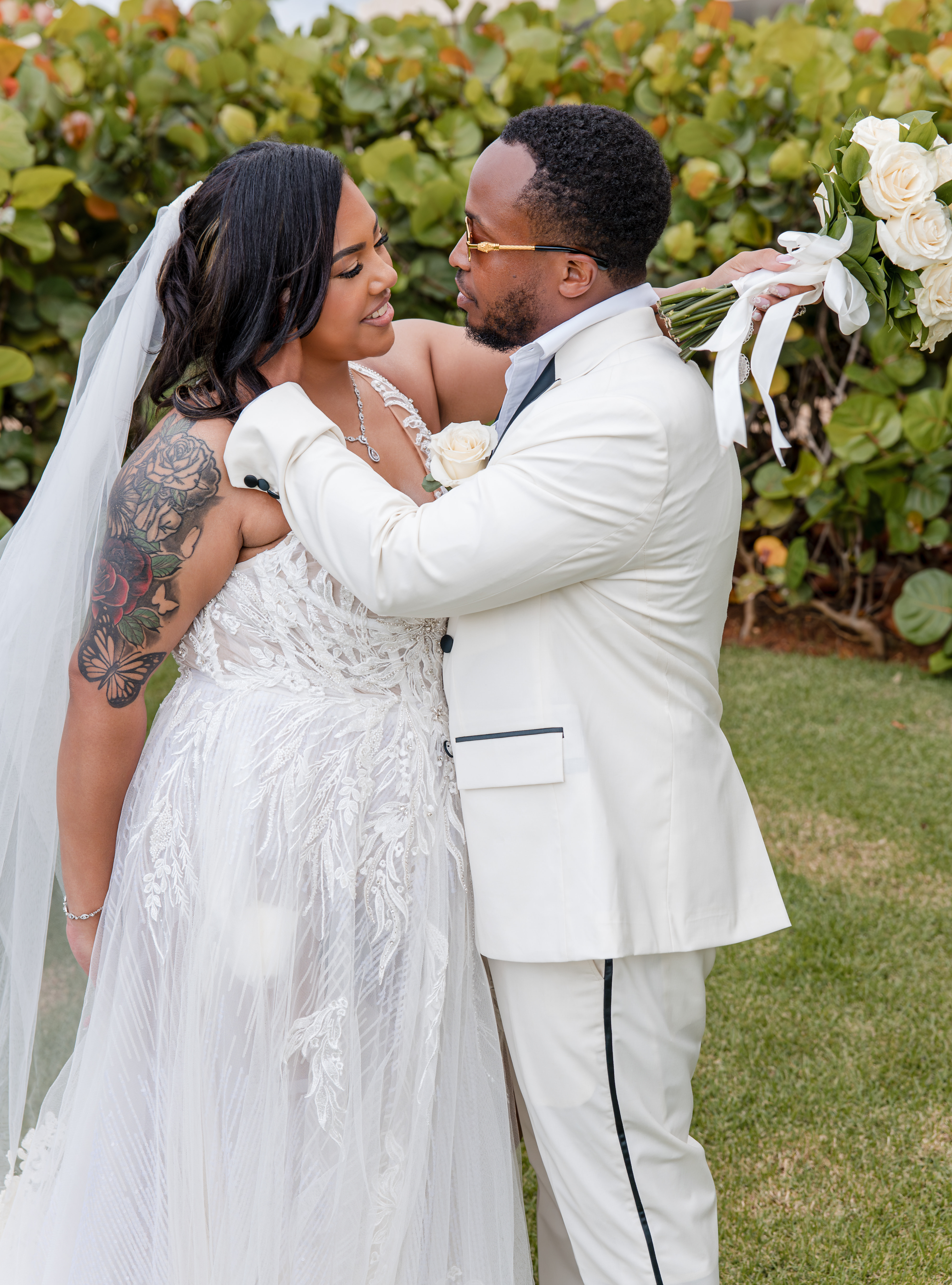 Leah and Ben embrace at their destination wedding outdoors, dressed in white and holding white roses.