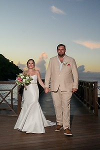 James and Brianna holding hands on a dock at sunset during their destination wedding, bride with bouquet.