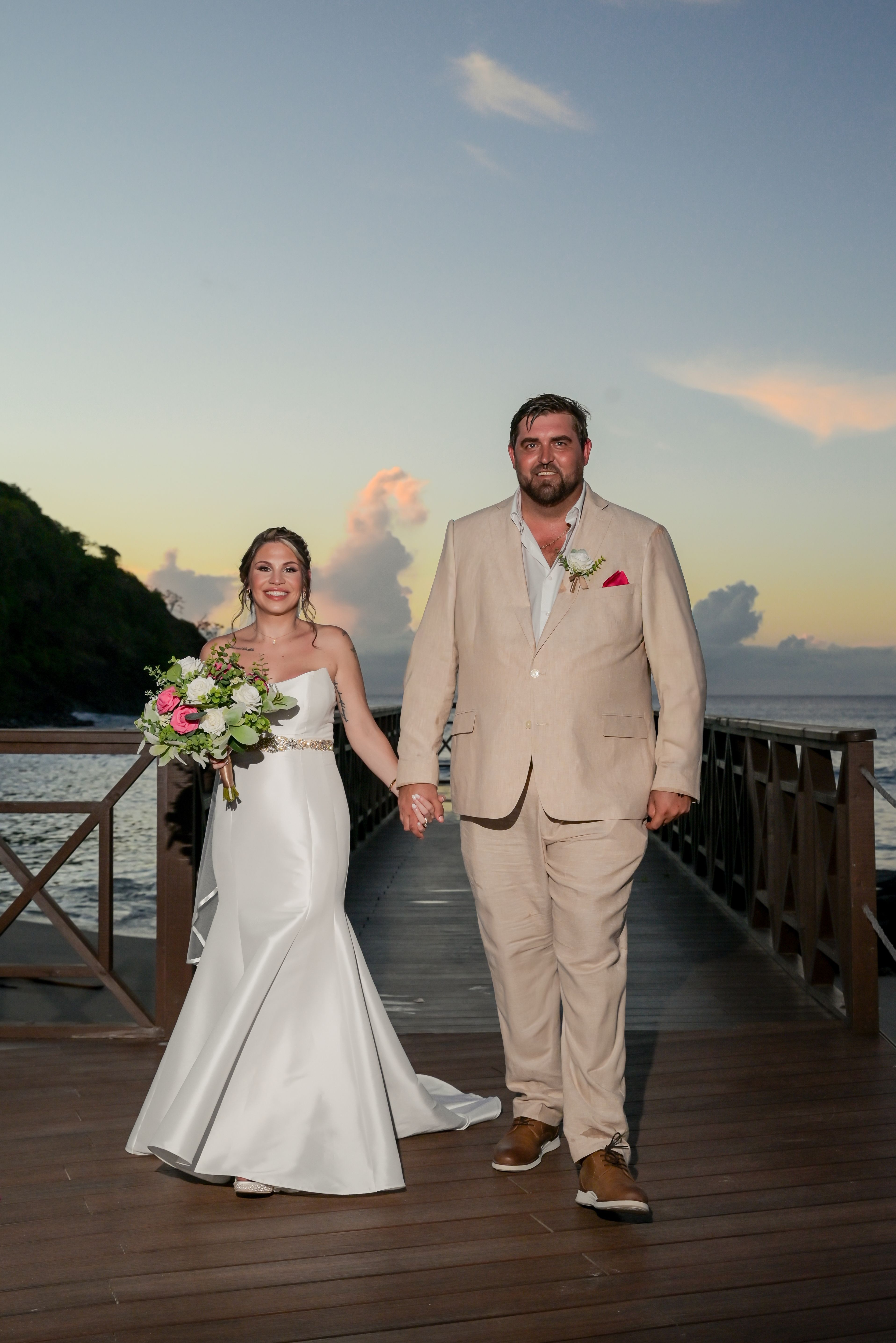 James and Brianna holding hands on a dock at sunset during their destination wedding, bride with bouquet.