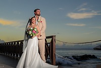 James and Brianna posing on a boardwalk by the ocean at sunset, holding a bouquet at their wedding.