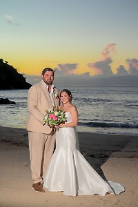 James and Brianna posing on a beach at sunset during their destination wedding, ocean in the background.