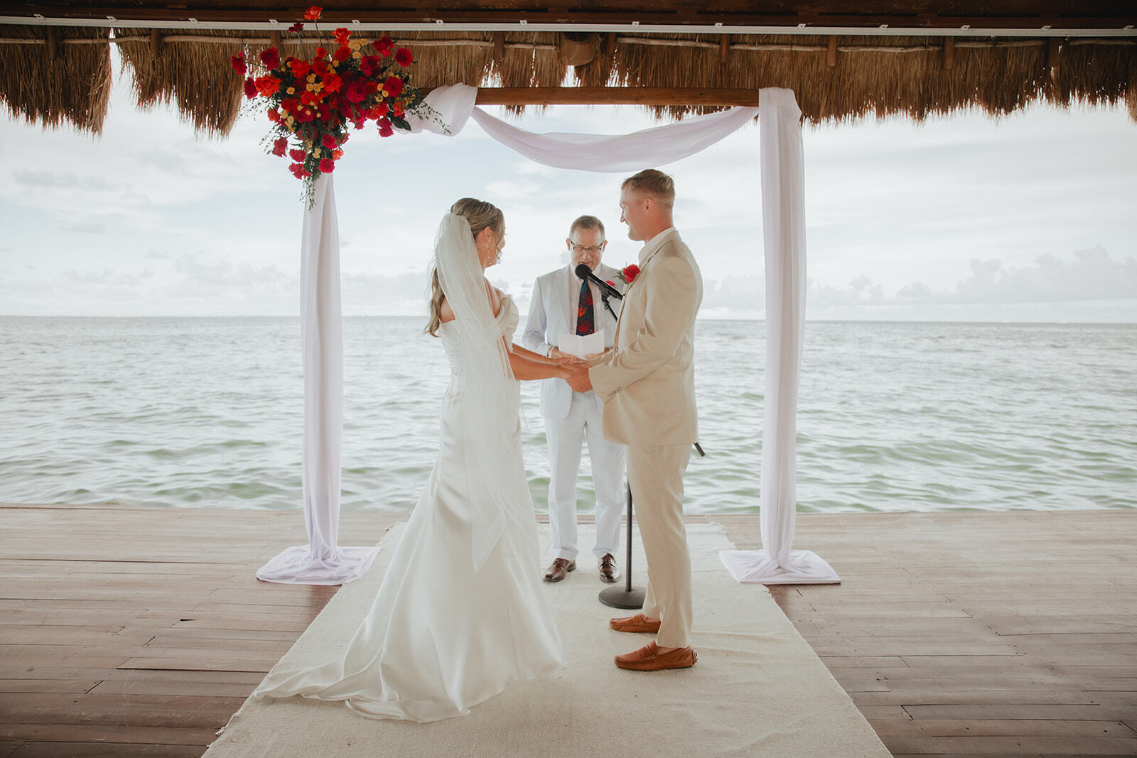 Kaitlyn and Chad face each other during a waterfront destination wedding ceremony outdoors.