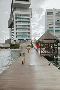 Kaitlyn and Chad stroll hand in hand on a dock by modern buildings at their destination wedding.