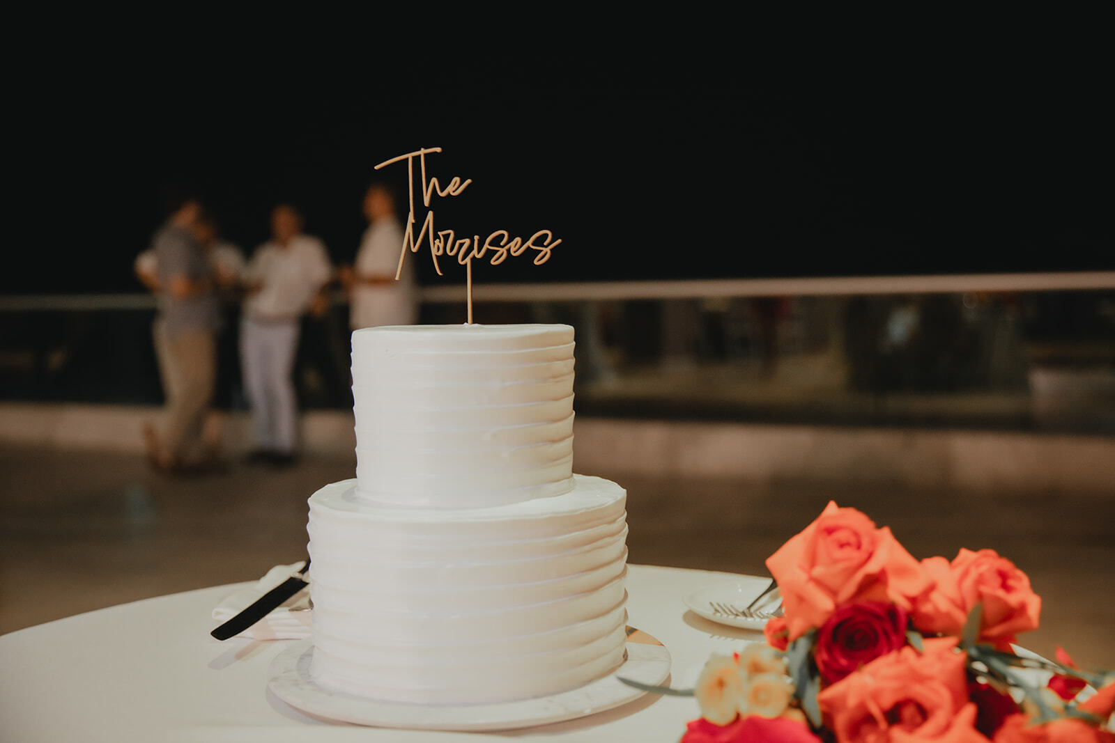 Two-tier white wedding cake with "Kaitlyn and Chad" beside orange roses, perfect for a destination wedding.