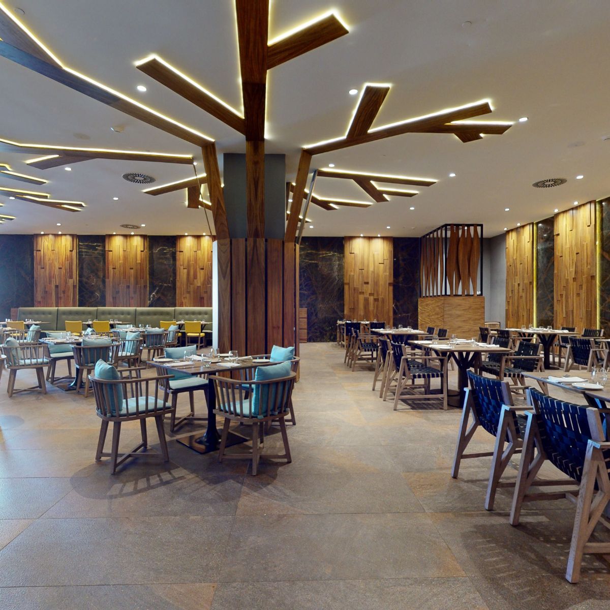 Modern restaurant interior with wooden decor, geometric lights, and tables set for a destination wedding.