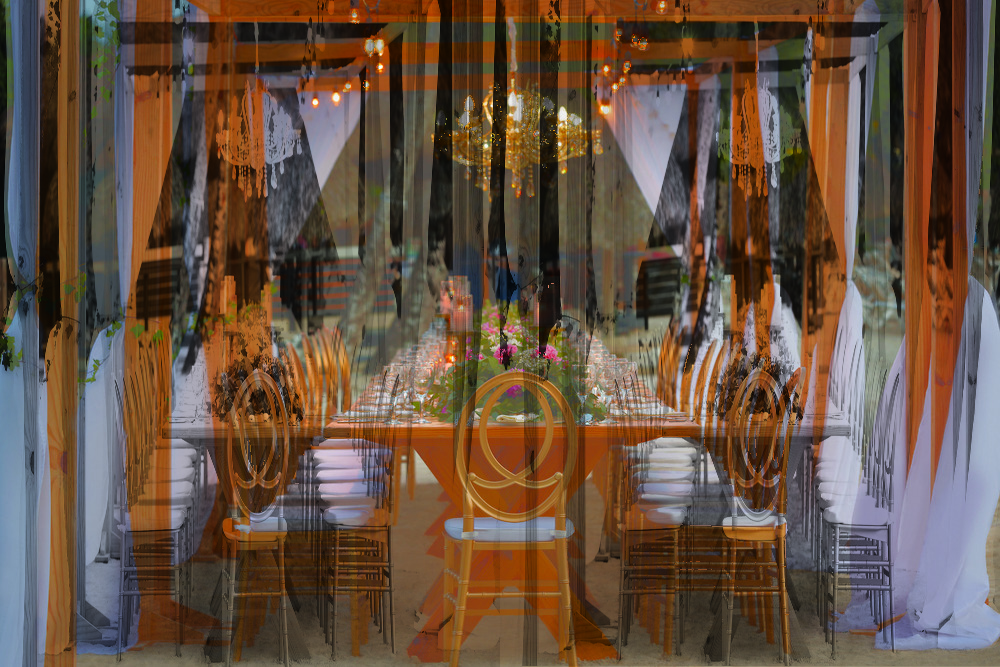 Elegant long wooden table arranged for a destination wedding dinner beneath a pergola with chandelier and candles.