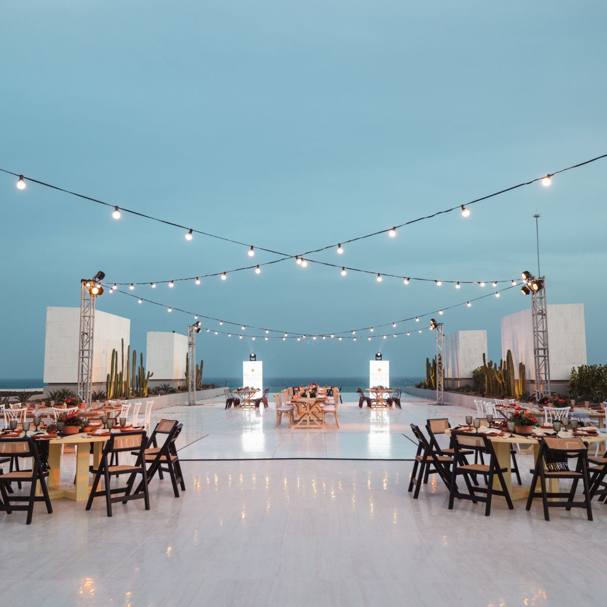 Rooftop destination wedding setup with string lights, chairs, and tables beneath a clear blue sky.