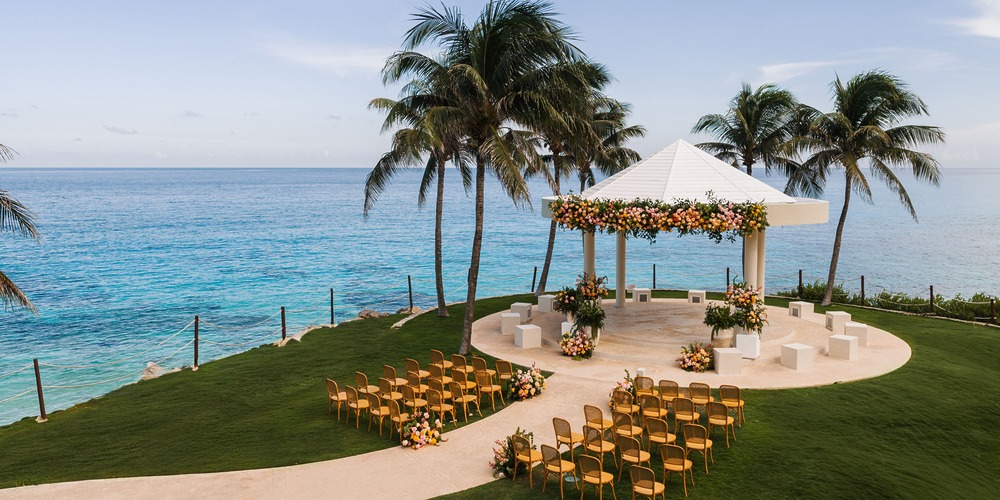 Destination wedding setup featuring rows of chairs and a flower-adorned gazebo facing the ocean.