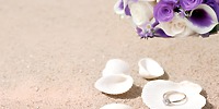 Wedding ring at Warwick Paradise Island Bahamas on seashells, white and purple flowers atop sand.