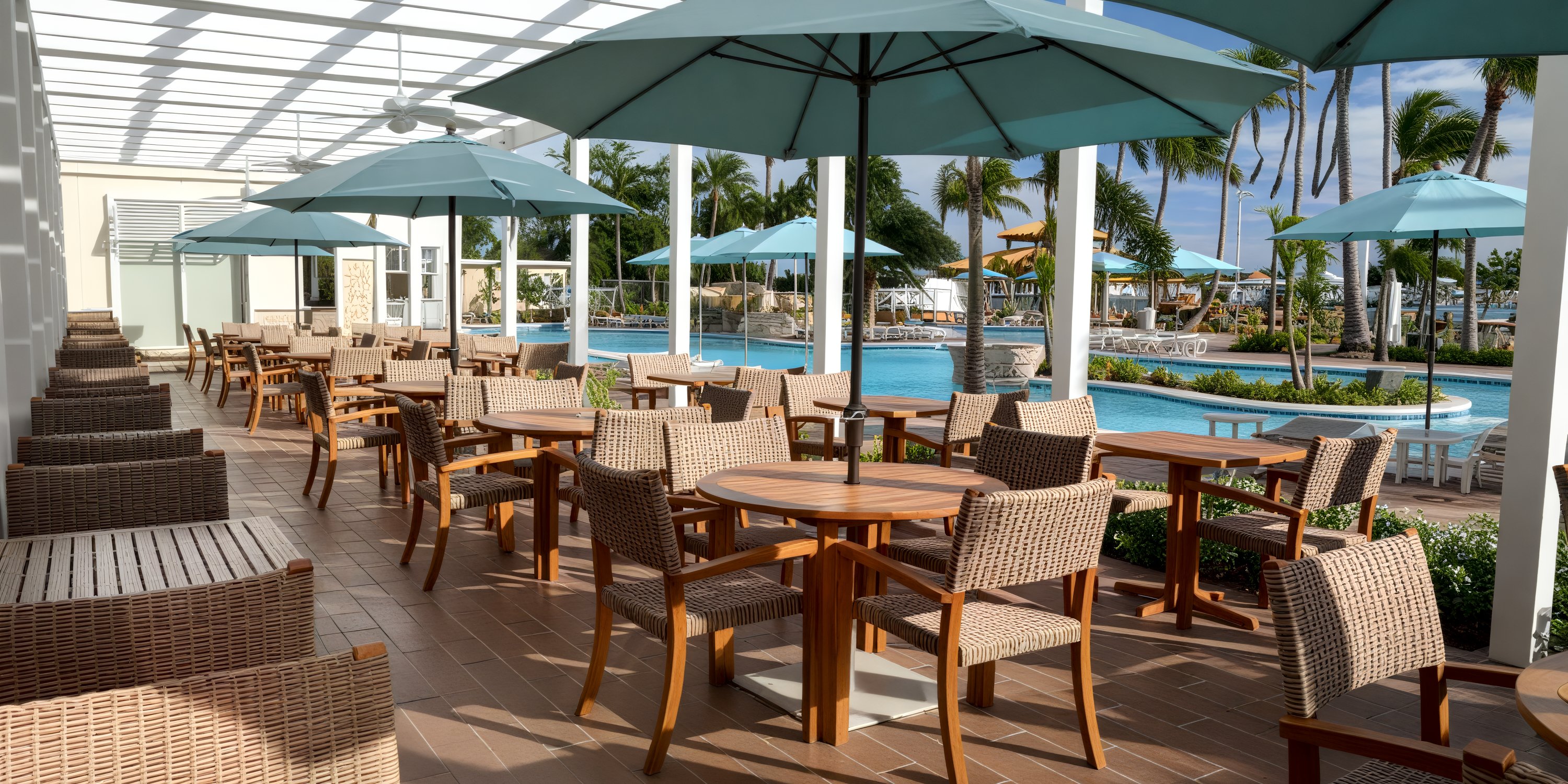 Wicker tables and chairs set for a destination wedding under umbrellas by the pool at Warwick Paradise Island.