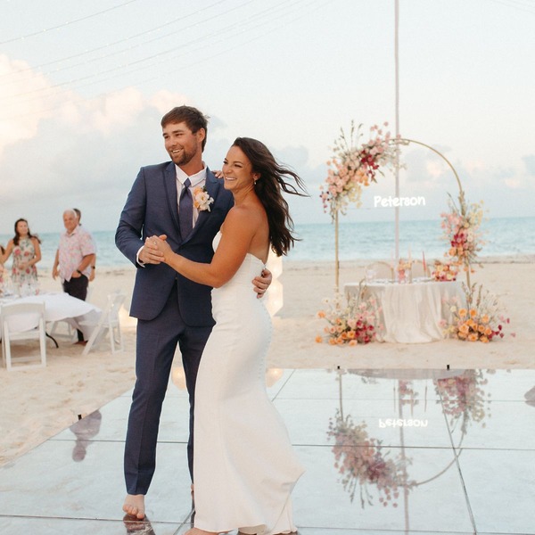 Bailey and Justin share a dance at their destination wedding, with an arch and table on the beach behind them.