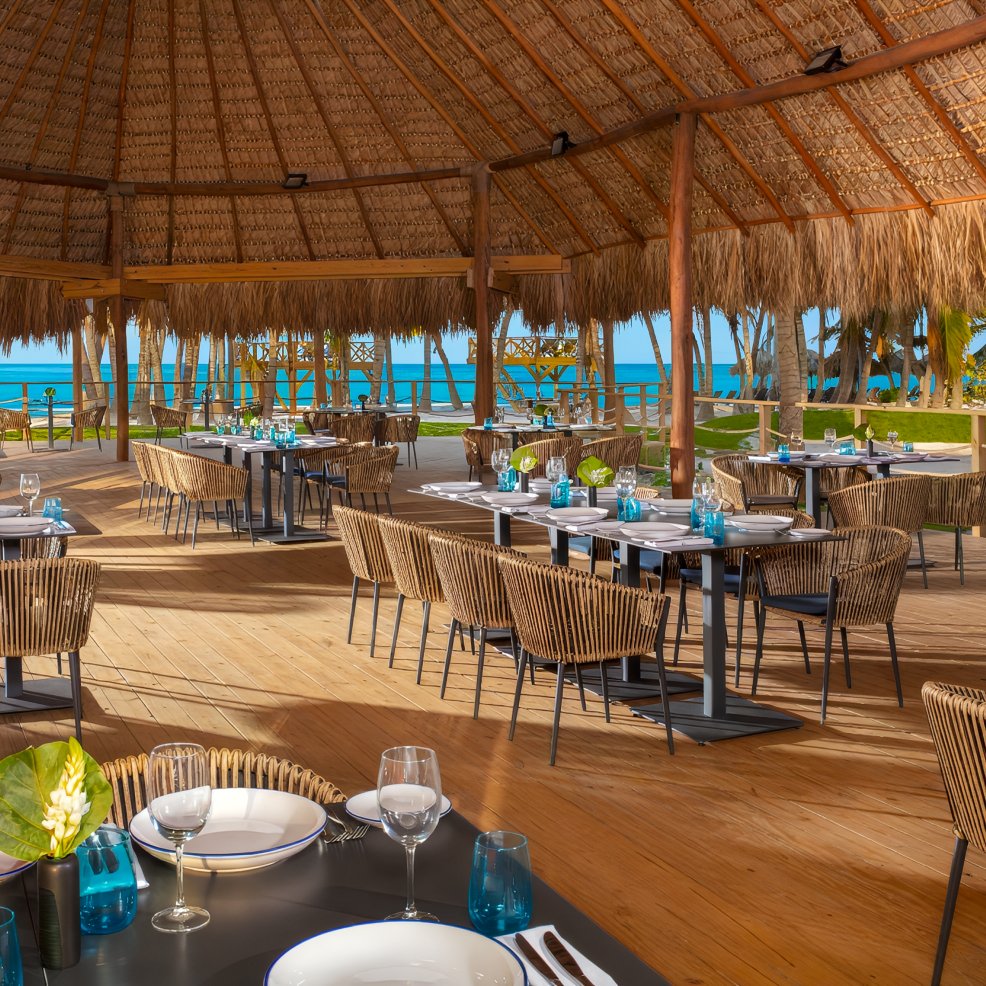 Outdoor restaurant with wooden floor and thatched roof, perfect for a destination wedding by the ocean.