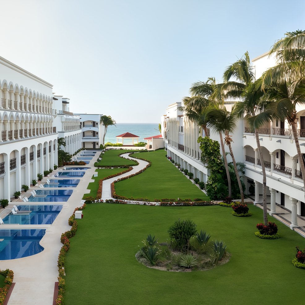Two white buildings with pools and green lawn, perfect for a destination wedding by the ocean under clear skies.