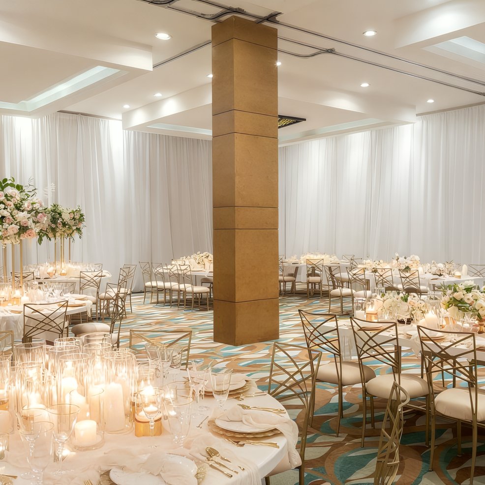 A wedding banquet hall featuring round tables, gold chairs, candles, and floral centerpieces.