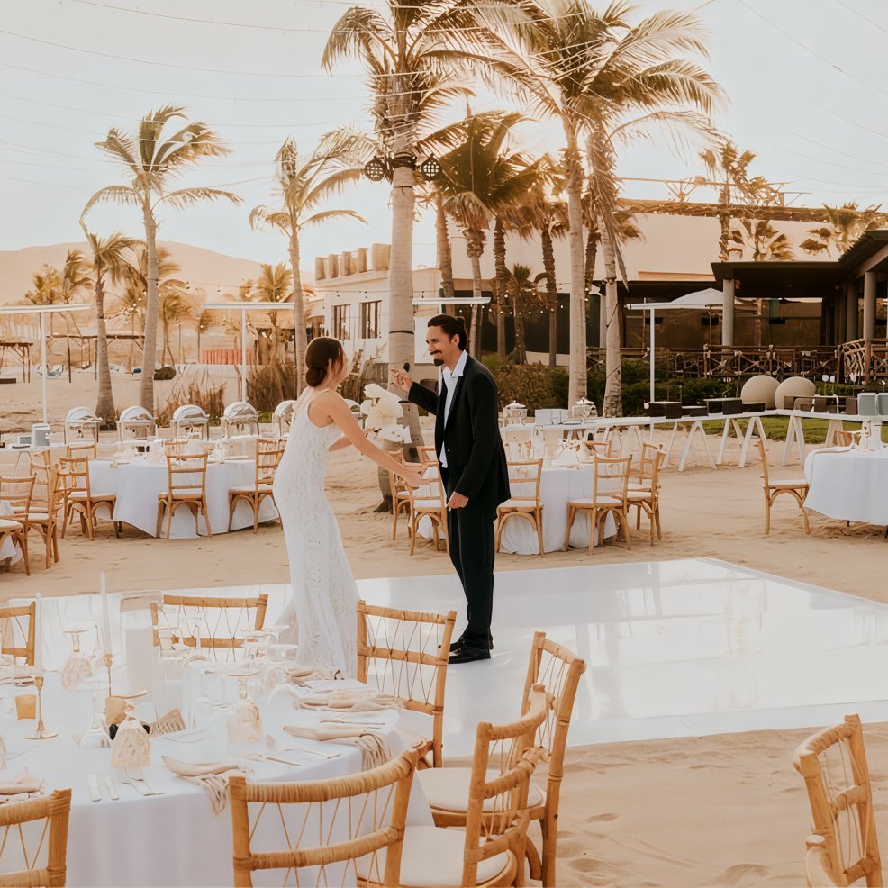A couple dances on a white floor at a beautiful destination wedding reception held on a sandy beach.