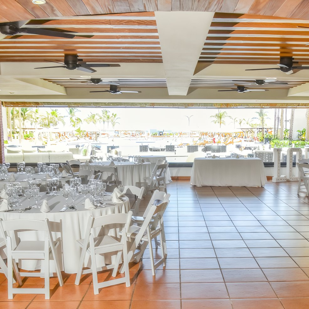 Indoor wedding banquet with round tables and chairs, offering views of a scenic destination beach.