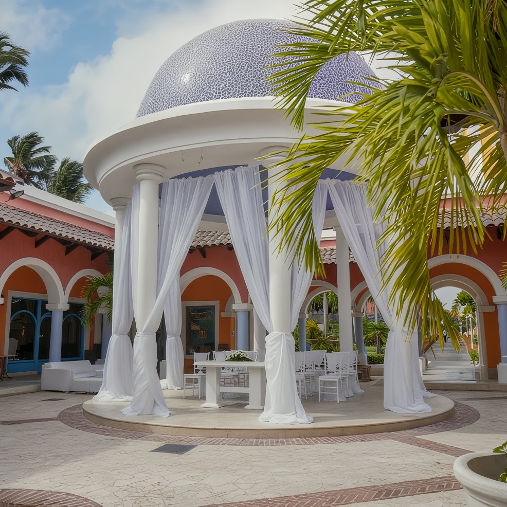 Elegant outdoor pavilion with white drapes and dome roof, perfect for a destination wedding amid palm trees.