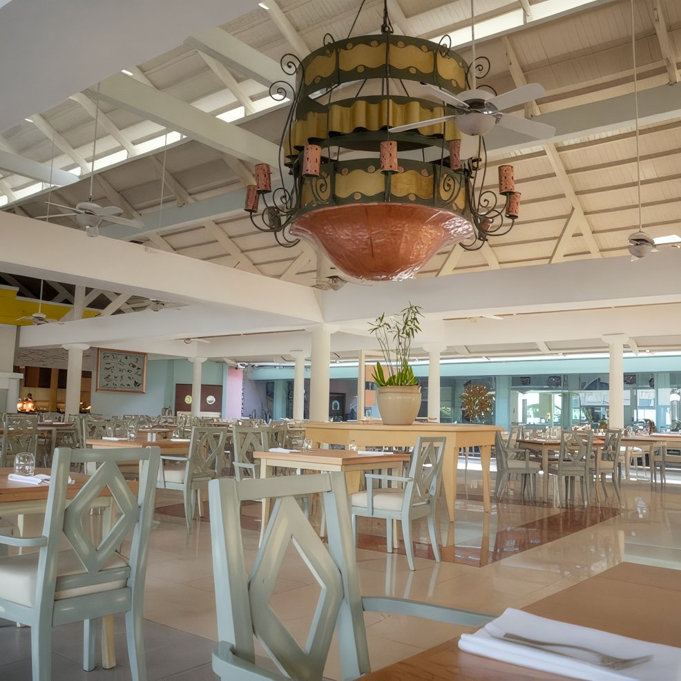 Spacious, empty restaurant with light tables and a grand chandelier, perfect for a destination wedding.