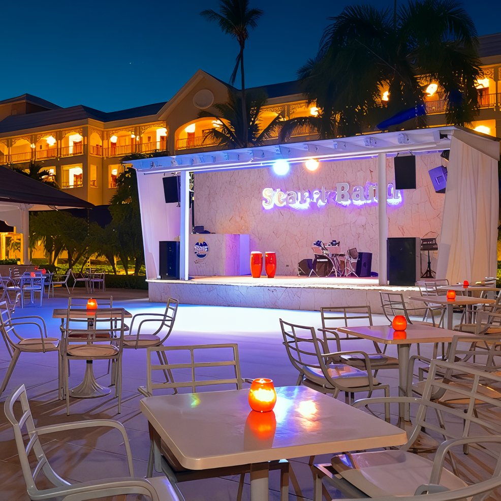 Outdoor bar stage at dusk set for a destination wedding, empty tables and chairs lit by candles and lights.