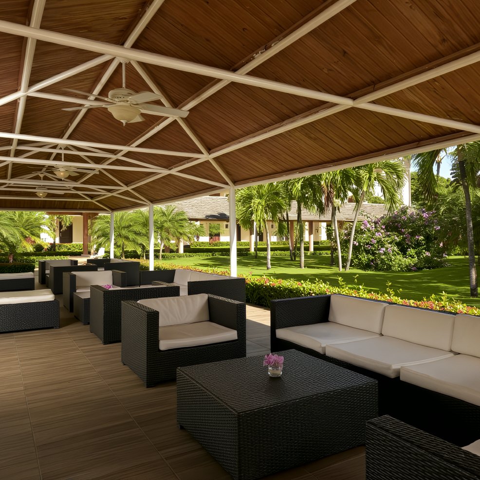Outdoor covered patio with black wicker sofas and tables, ideal for a destination wedding, garden view.