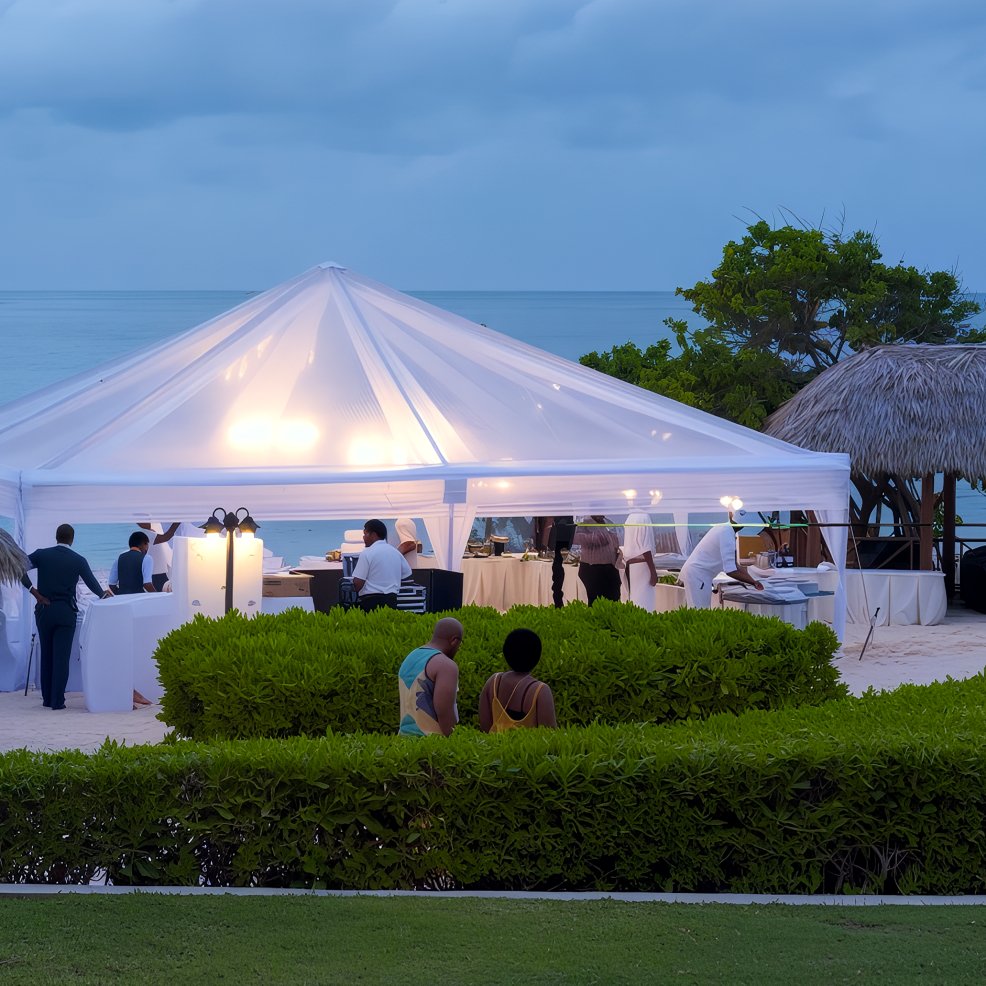 White tent arranged for a destination wedding on the beach, with guests mingling and catering staff nearby.