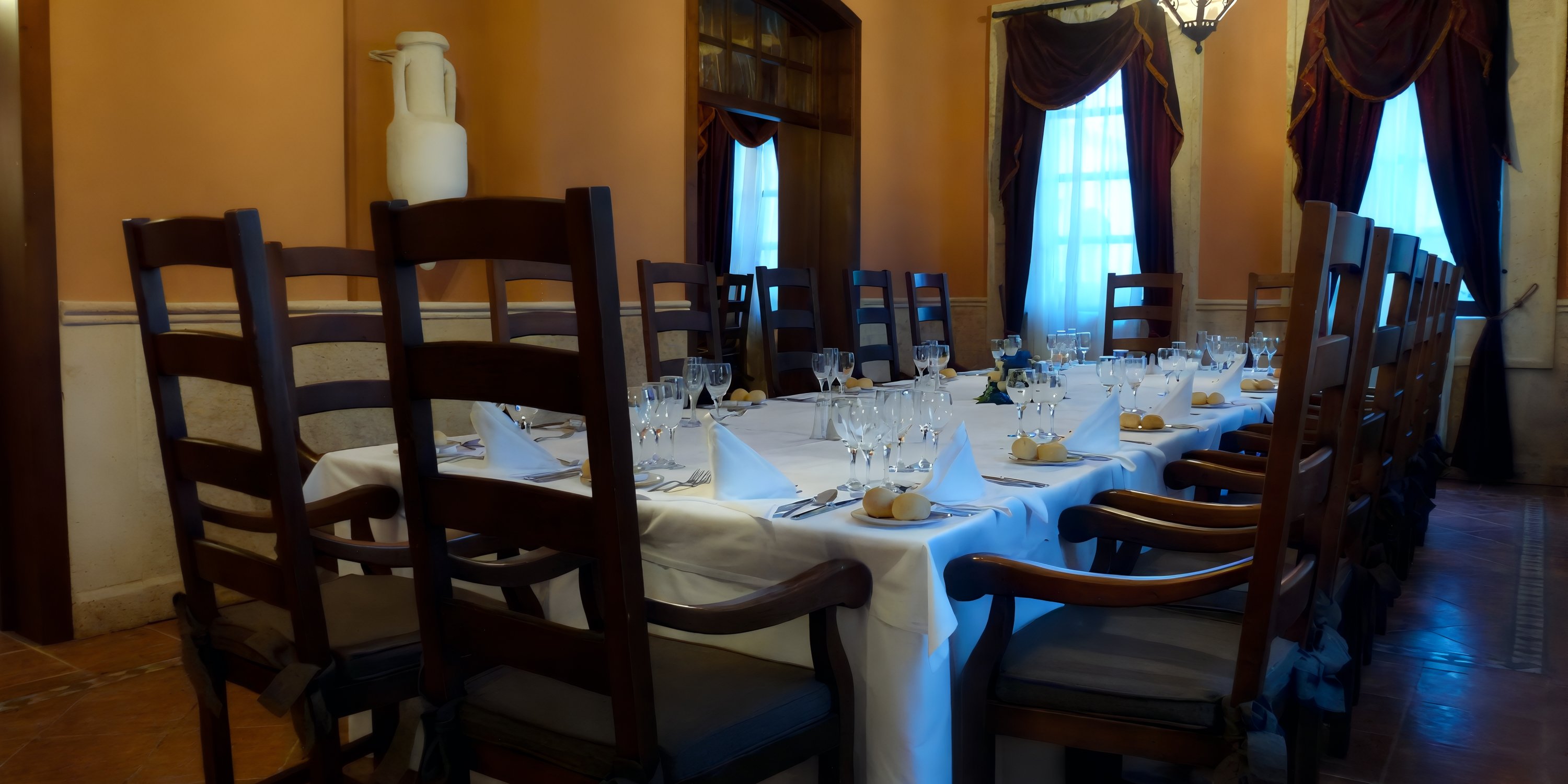 Elegant wedding dining table set with glassware, plates, and napkins in a room with tall chairs.