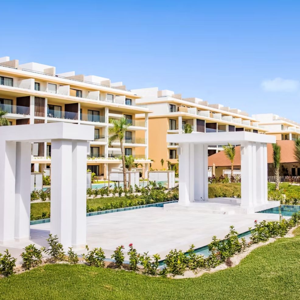 Modern hotel buildings with balconies and a white pavilion, ideal for a destination wedding, under blue sky.