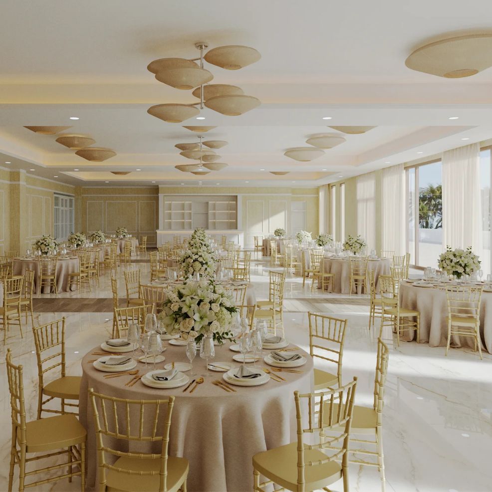 Sophisticated banquet hall set for a destination wedding, with gold chairs and floral centerpieces on tables.