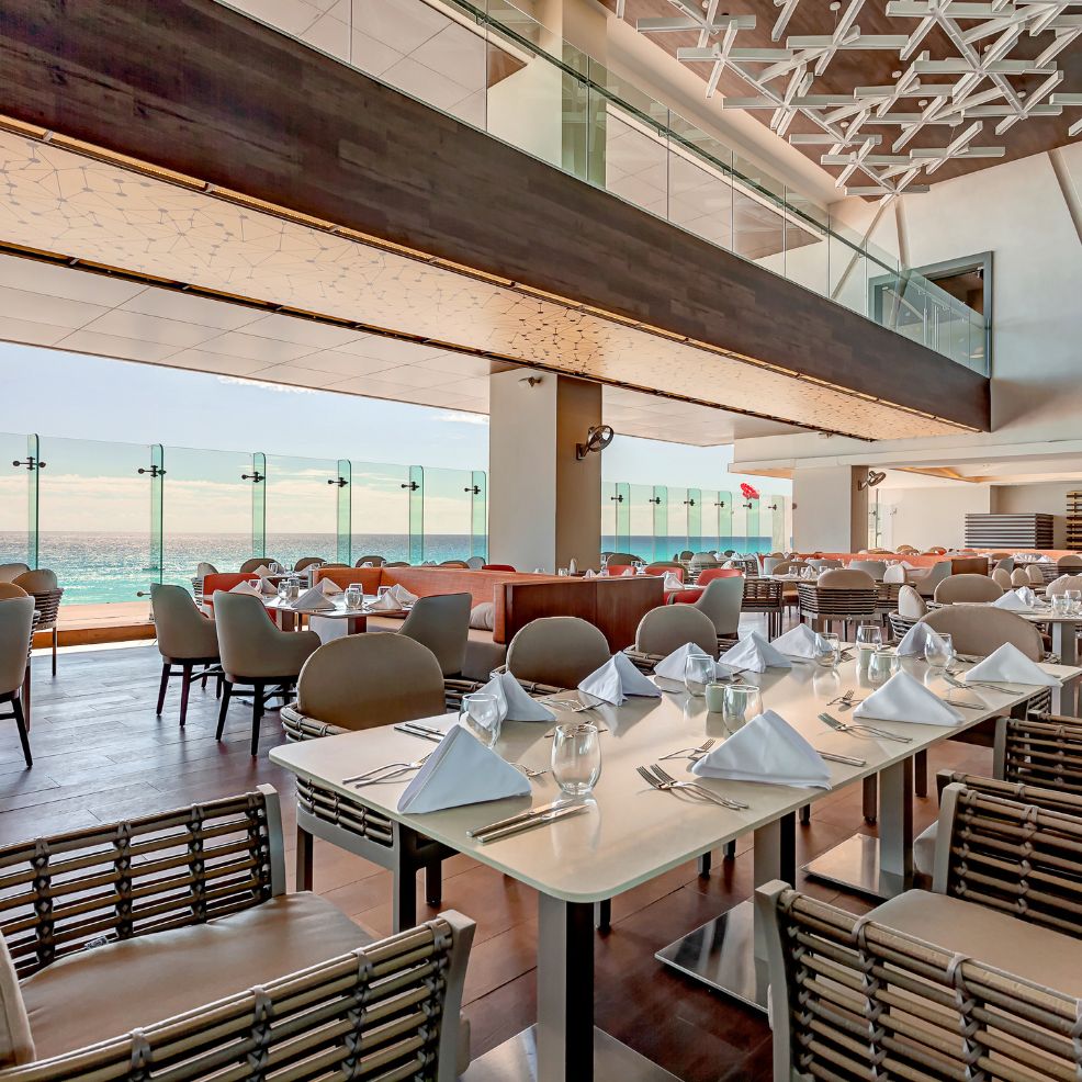 Chic restaurant with ocean views, set for a destination wedding, featuring floor-to-ceiling windows.