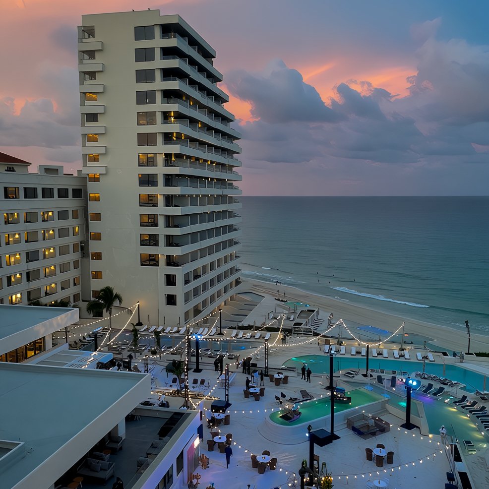 A destination wedding venue by the ocean at sunset, with a pool area aglow under string lights.