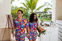 A couple in matching tropical outfits holds hands, one with a bouquet, at a destination wedding.