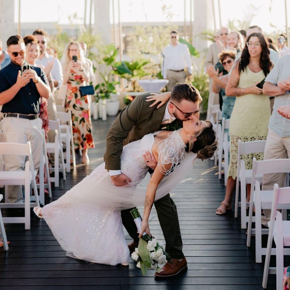 Shirley and William share a kiss at their destination wedding as smiling guests snap photos.