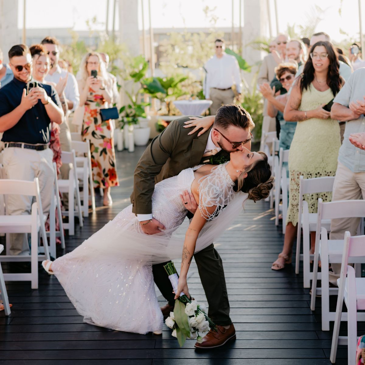 Shirley and William share a kiss at their destination wedding as smiling guests snap photos.