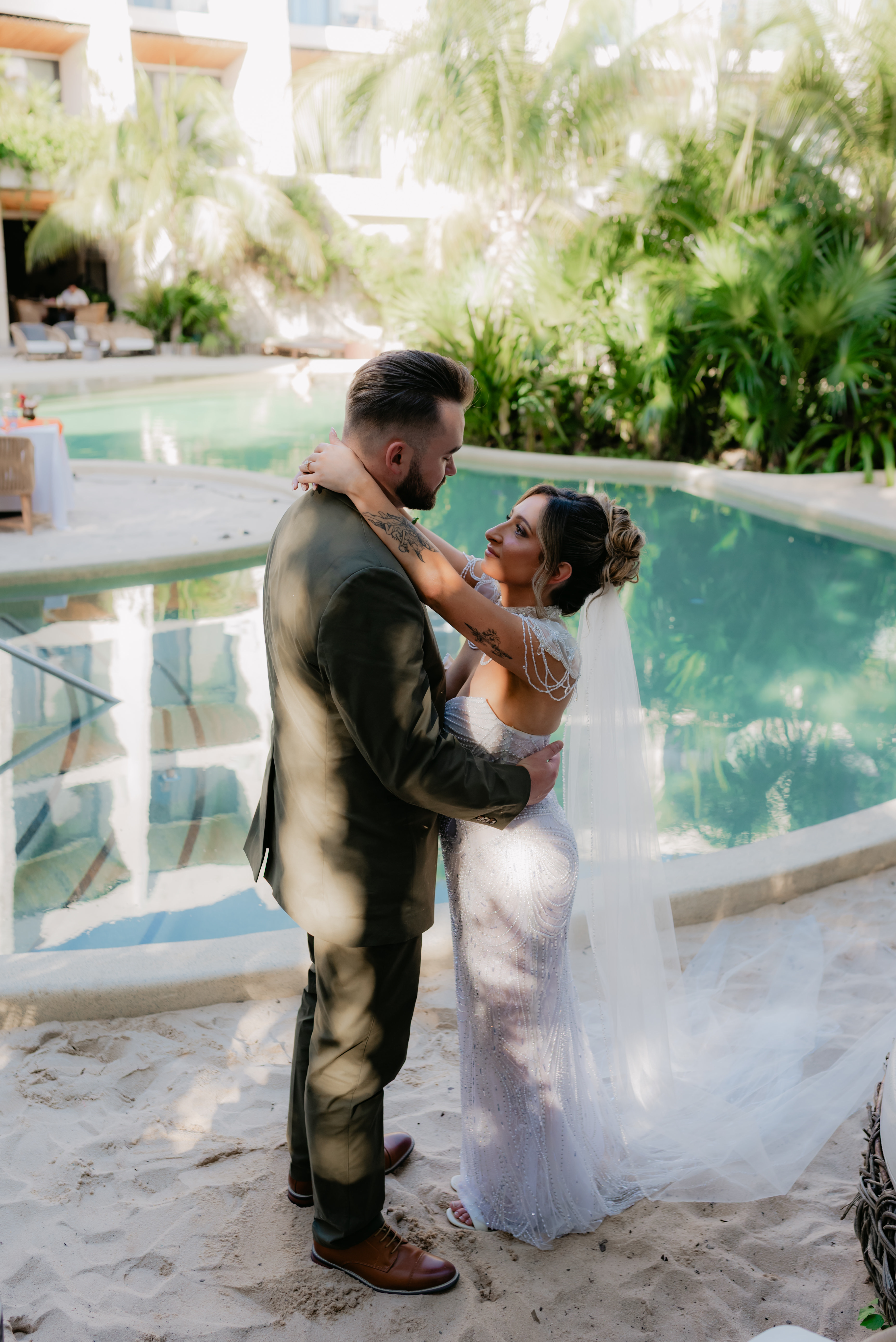 Shirley and William embrace by a poolside on a sunny day, celebrating their destination wedding.