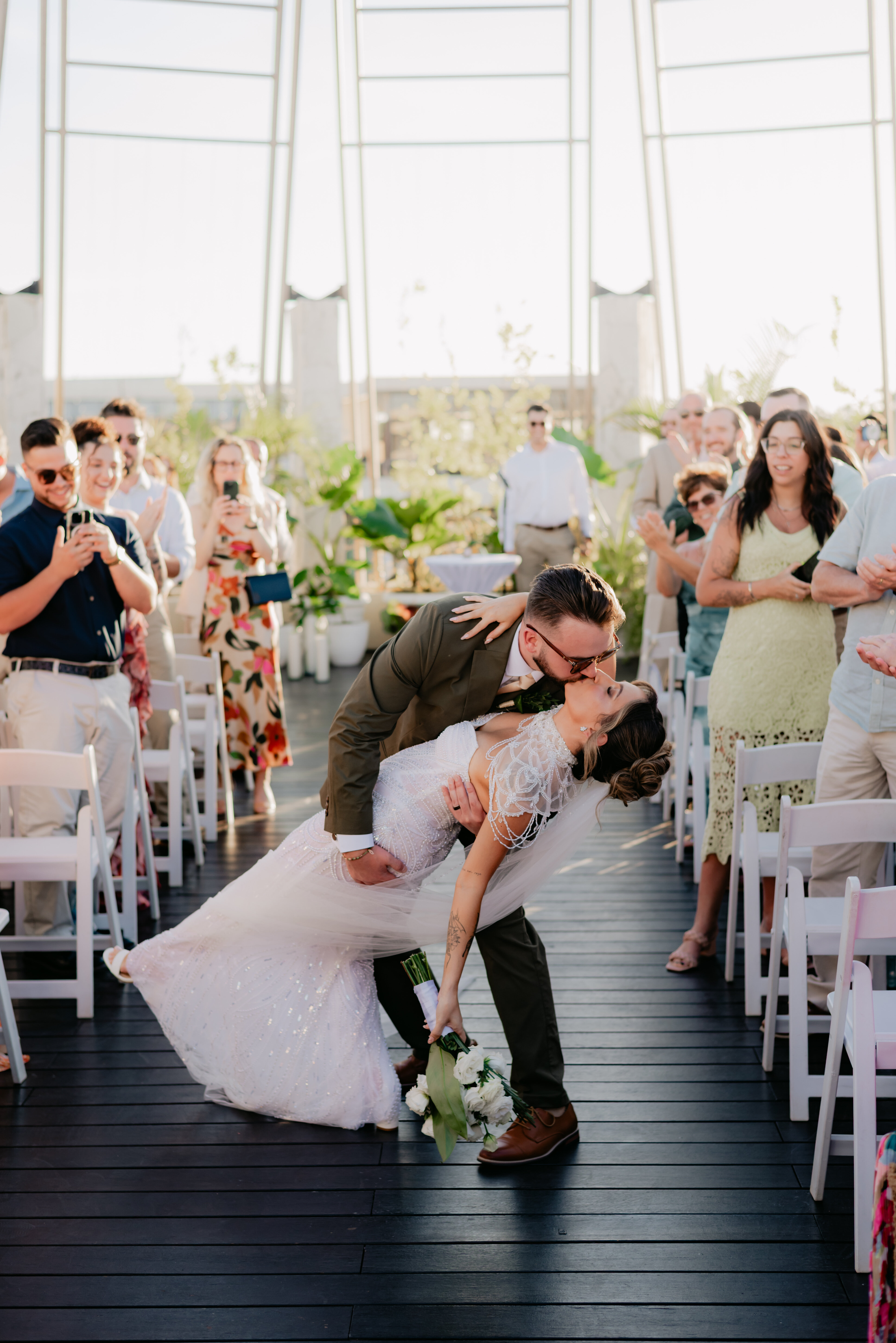 At their indoor wedding, Shirley and William share a dip and kiss while guests watch and take photos.