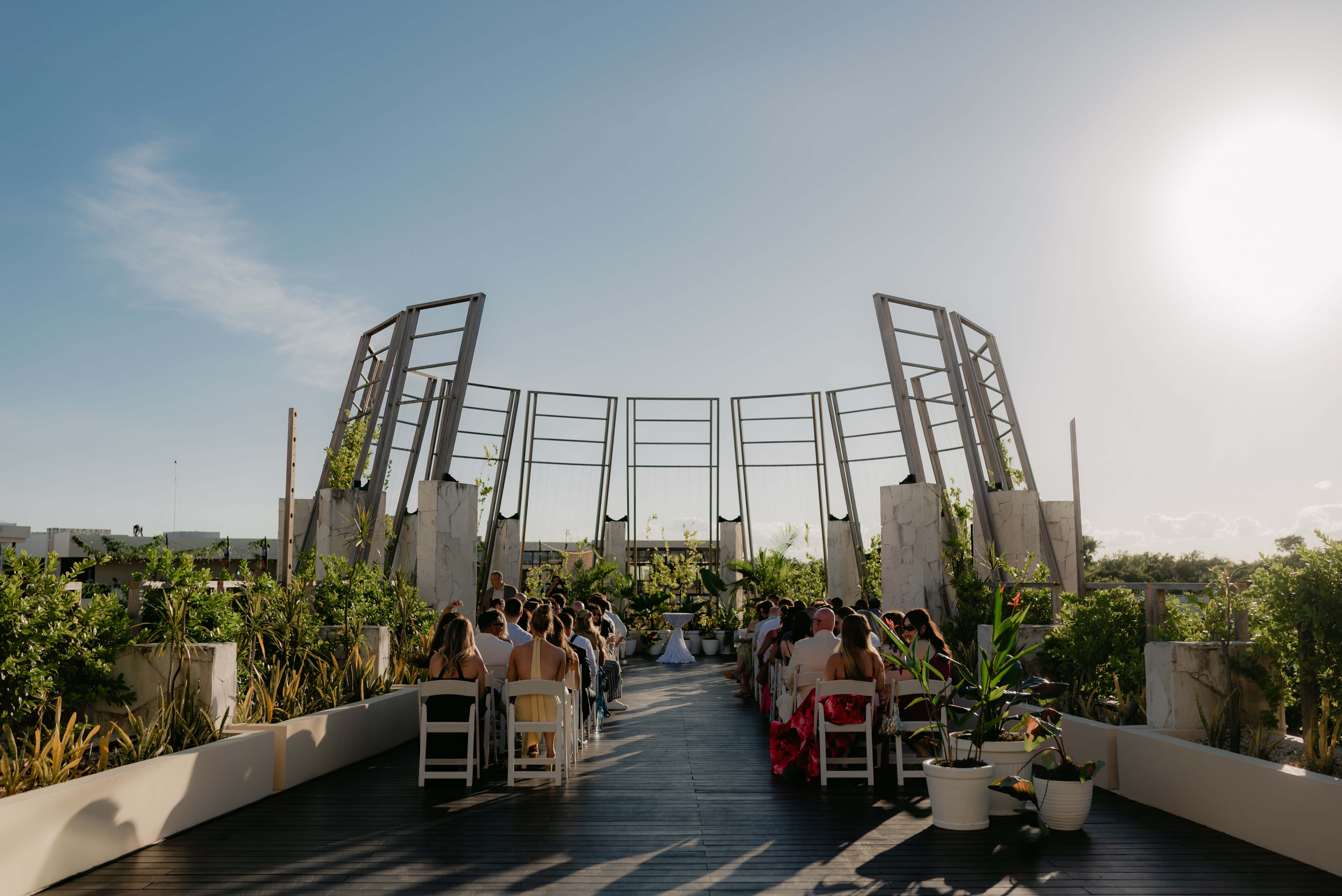Outdoor destination wedding: Shirley and William seated beneath a modern open-air structure on a sunny day.