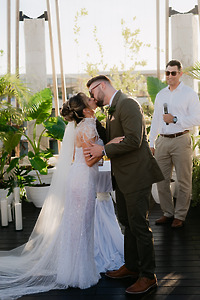 Shirley and William (Copy) share a kiss at their outdoor wedding as the officiant looks on.
